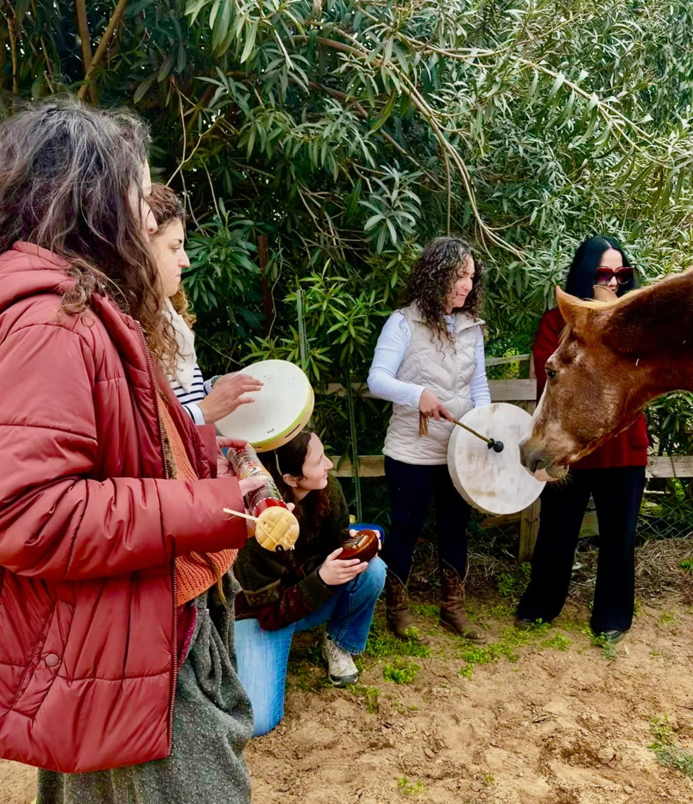 Women holding drums and instruments beside a chestnut horse